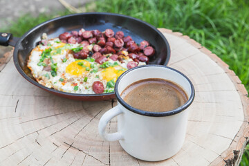 breakfast in the forest: scrambled eggs with sausage and coffee in the foreground