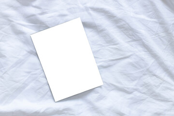 Blank flyer poster mocap on white sheet bed background with copyspace, top view, flat lay