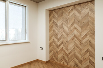 part of living room with a finishing wall imitating wooden parquet near the white wall with a window