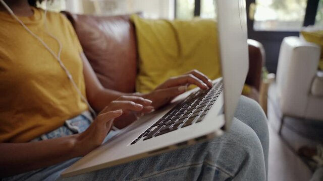 Close-up of woman in casualwear sitting on sofa busy in typing on laptop at home