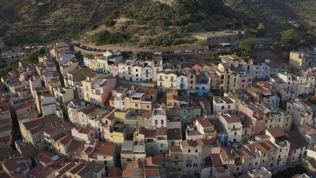 Aerial pan shot city view for buildings surrounded by green mountains and a canal river during sunset. Bosa, Sardinia, Italy and Temo river.