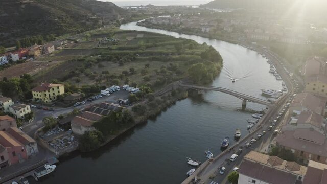 Static aerial shot for one speed boat running on Temo River of Sardinia and passing under a canal bridge with parked boats during sunset.
