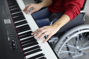 Woman in wheelchair is pressing piano keys close-up. Hobbies of people with disabilities concept.