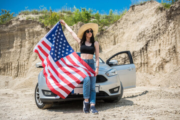 Photo shoot of a charming lady with the USA flag near the car in a sand quarry