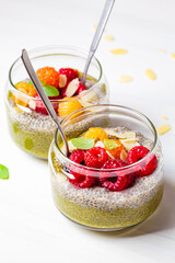 Green matcha tea chia seeds pudding with raspberries in a glass jar, white background.