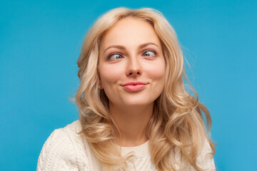 Closeup beautiful woman with curly blond hair having fun crossing her eyes, fooling face, crazy positive mood. Indoor studio shot isolated on blue background