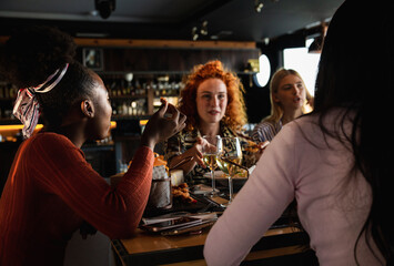 Group of young female friends having fun in restaurant, talking and laughing while dining at table.