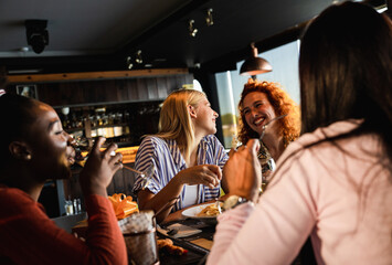 Group of young female friends having fun in restaurant, talking and laughing while dining at table.