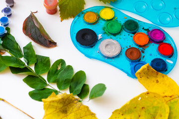 girl drawing with paint on fall leaves at table.