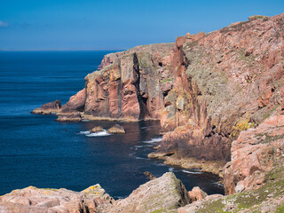 Fototapeta na wymiar Red granite cliffs on Muckle Roe, Shetland, UK - these rocks are of the Muckle Roe Intrusion - granite, granophyric - igneous bedrock formed 359 to 383 million years ago in the Devonian Period.