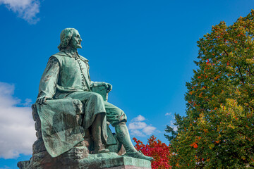 Fototapeta premium Statue of great scientist Otto von Guericke in red and golden Autumn colors in historical downtown of Magdeburg Germany, at sunny day and blue sky, closeup, details..