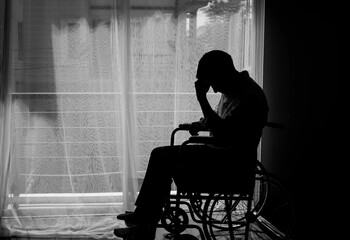 Silhouette of handicapped Man sitting on wheelchair in front of a large panoramic window in...