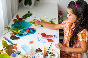 Little girl painting on autumn yellow leaves with gouache, kids arts, children creativity, autumn art.