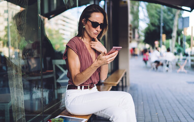 Thoughtful adult lady using smartphone on street