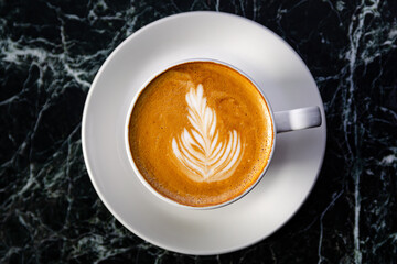 Cup of delicious coffee with latte art top view. White cup and saucer ona dark marble counter.