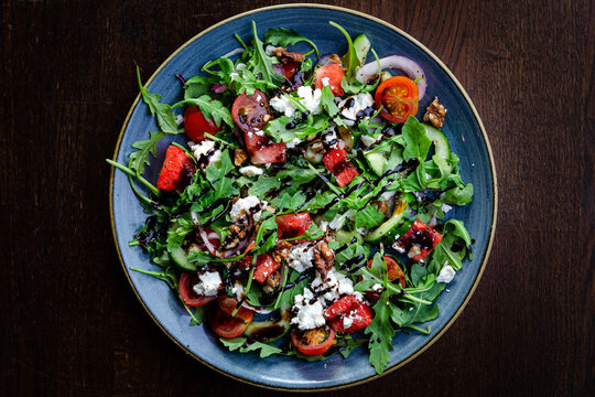 Watermelon and ricotta salad with walnuts, rocket, cherry tomatoes, cucumber and balsamic vinaigrette on a blue plate top view