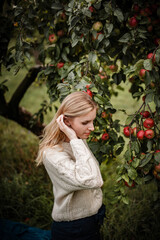 Autumn vibes - blonde woman is posing around apple tree full of red apples