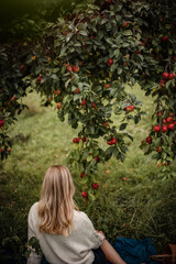 Young woman with beautiful healthy hair is sitting under apple tree on a sunny autumn day