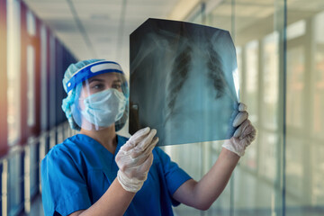 young nurse in  blue uniform protective mask face shield looks at the result of lung fluorography