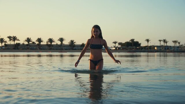 Beautiful teenager girl walking in sea at sunset beach in Hurghada resort.