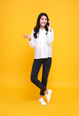Fototapeta na wymiar Smiling young casual Asian woman talking smart phone isolated over yellow background.