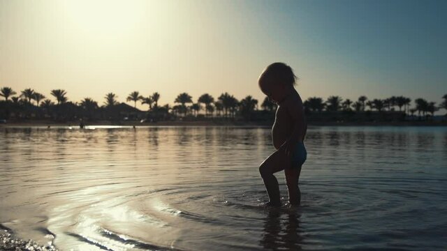 Cute toddler walking in seawater at beach. Little child playing at seaside.
