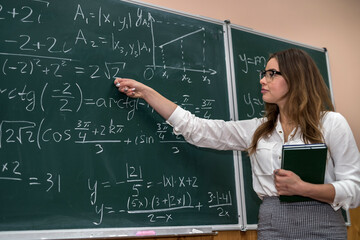 Young teacher writing and explain the mathematical formulas on a chalkboard