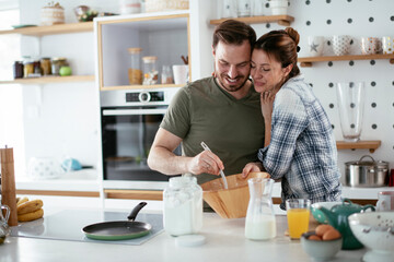 Fototapeta na wymiar Young couple making pancakes at home. Loving couple having fun while cooking..