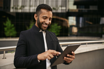 Dapper smiling indian muslim businessman using digital tablet outside