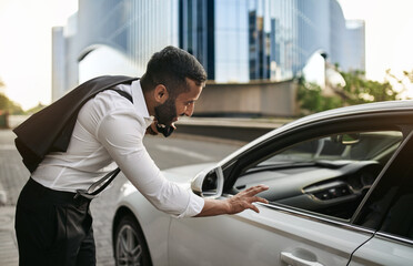 Fototapeta na wymiar Bearded Indian Muslim businessman talking to taxi Driver in city