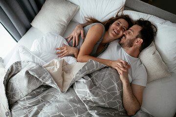 Naklejka na ściany i meble Young loving couple in bed. Happy couple relaxing in bed.