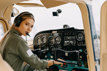 Confident woman pilot in airplane cockpit, wearing headset, looking at camera. © Bostan Natalia