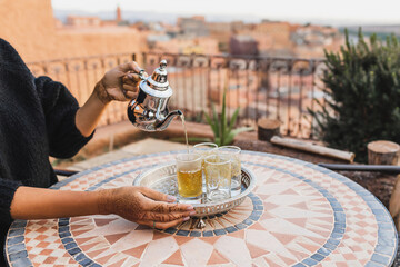 Woman hand pouring traditional moroccan mint tea in glasses. Vintage silver tray and teapot. Round mosaic table. Morocco hospitality. - obrazy, fototapety, plakaty