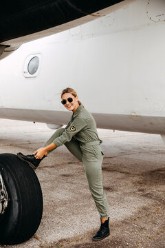 Woman pilot wearing uniform, smiling, tying laces on her boots with foot on plane tire.