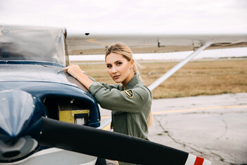 Confident woman pilot wearing uniform, standing next to a private airplane, looking at camera.