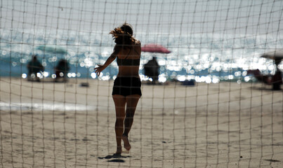 A female beach volleyball player in action behind a web.