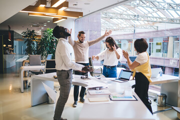 Happy diverse male and female colleagues dressed in smart casual clothing celebrating completed project in office workspace, excited partners satisfied with brainstorming meeting for cooperation