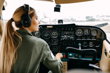 Woman pilot sitting in airplane cockpit, wearing headset. - obrazy, fototapety, plakaty