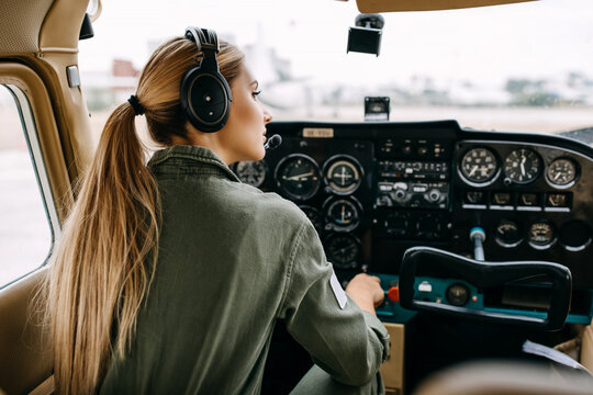 Woman pilot sitting in airplane cockpit, wearing special headset.