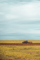 Tractor plowing the fields in the countryside. Agricultural tractor plowing the field. Red Tractor with plow.