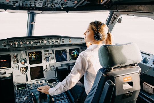 Woman pilot sitting in airplane cockpit, wearing headset.