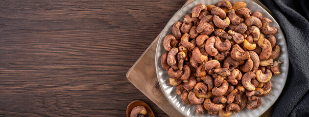 Obraz na płótnie Canvas Cashew nuts with peel in a plate on wooden tray and table background, healthy raw food plate.