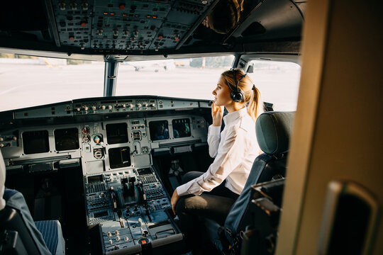 Woman pilot sitting in aircraft cockpit, wearing headset.