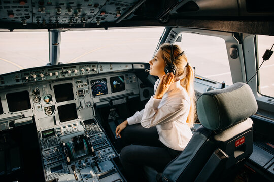 Woman pilot sitting in aircraft cockpit, wearing headset.