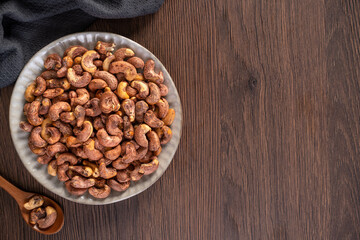 Cashew nuts with peel in a plate on wooden tray and table background, healthy raw food plate.