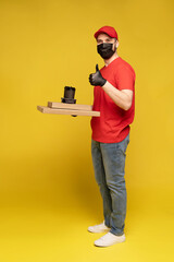 Delivery man in red cap, t-shirt uniform, protective mask and gloves isolated on yellow background studio. Guy hold takeaway cup of coffee