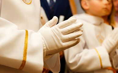 Hands of a praying child during the liturgy in the Catholic Church. The boy during the first communion. Boy's hands in white gloves.