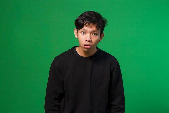 asian young man with blank shocked expression. isolated on green background