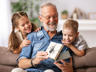 Happy family aged grandfather and grandchildren girl   and boy opening gift box while resting on...