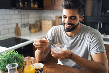 Attractive bearded man sitting at his nice kitchen table, eating cereals for breakfast